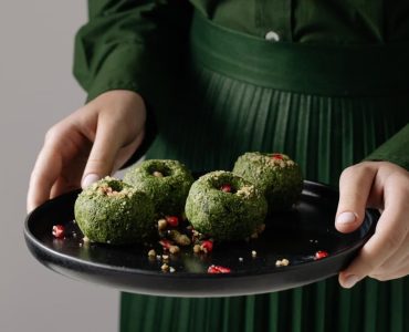 Delicious Georgian spinach pkhali on a black plate, held by a person in green attire.