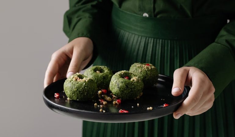 Delicious Georgian spinach pkhali on a black plate, held by a person in green attire.