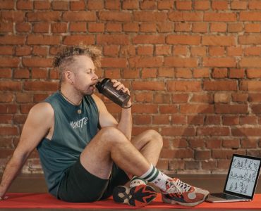 Athletic man sitting on exercise mat with water bottle, taking a break from workout, in a rustic indoor setting.