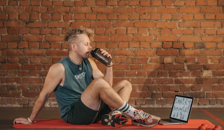 Athletic man sitting on exercise mat with water bottle, taking a break from workout, in a rustic indoor setting.